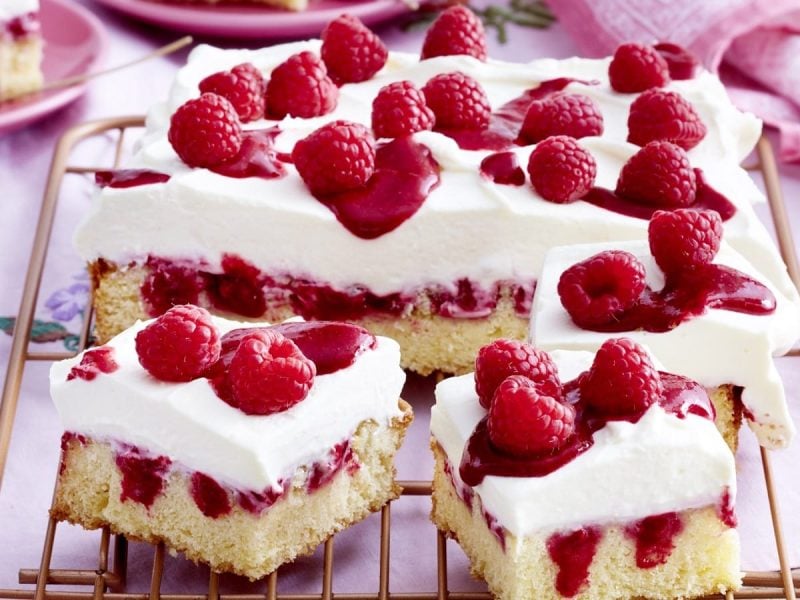 Auf einem Blech liegt ein Himbeer-Mascarpone-Kuchen. Er ist mit einer Creme und Himbeeren verziert.