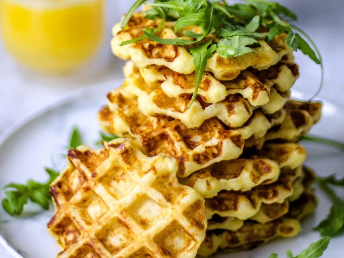 Auf einem Teller liegen mehrere Kartoffelwaffeln mit Rucola und Orangensaft. Sie sind mit Rucola belegt.