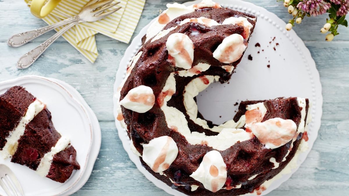 Auf einem weißen Teller liegt eine Kiba-Gugelhupftorte. Sie ist mit Sahne betupft und mit Creme gefüllt.