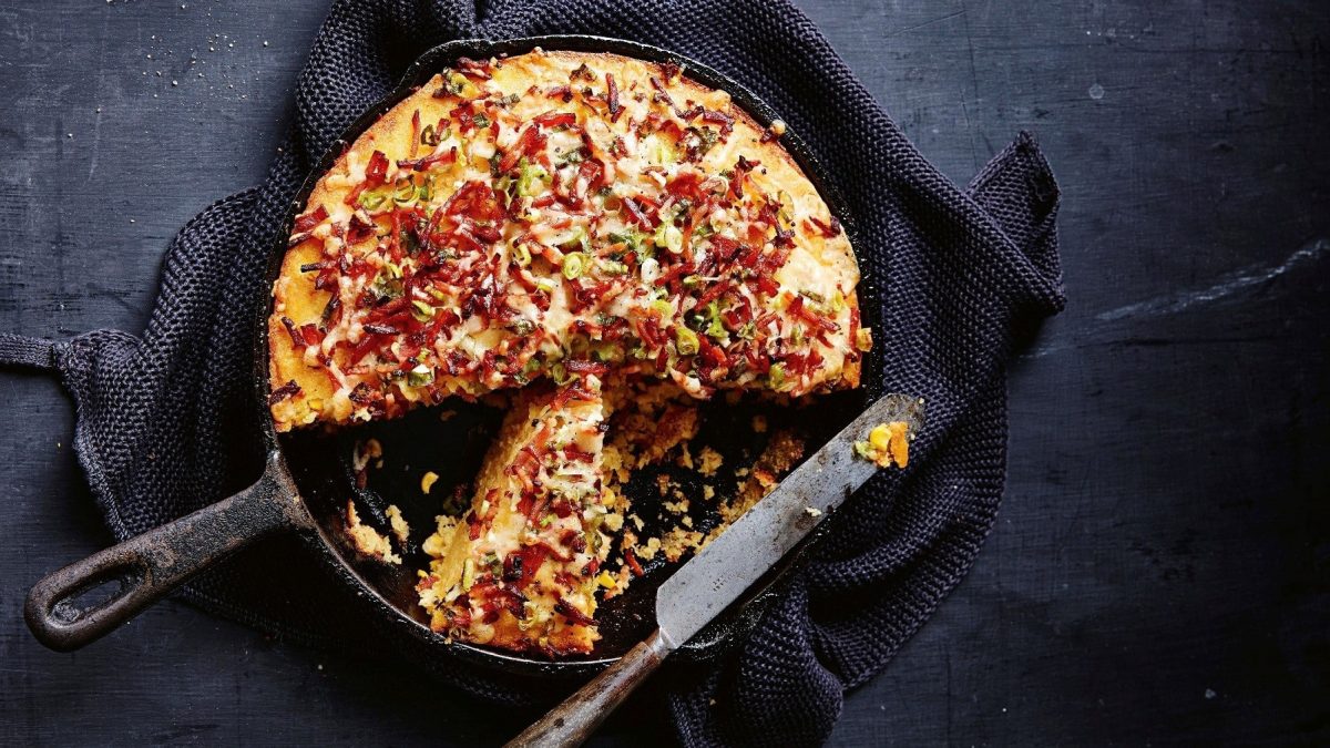 Maisbrot mit Speck und Käse, gebacken und serviert in einer gusseisernen Pfanne auf einem schwarzen Schiefertisch.