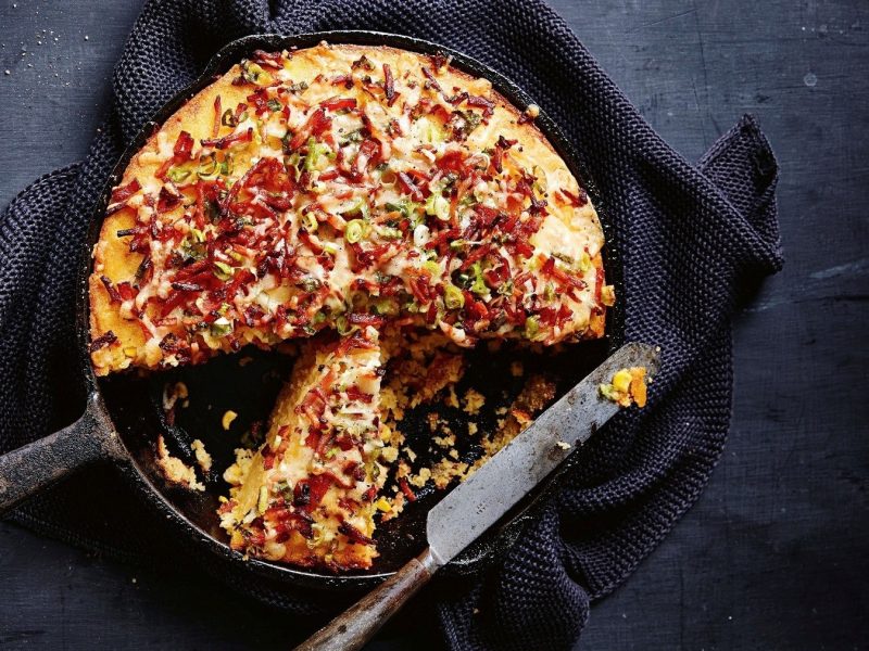 Maisbrot mit Speck und Käse, gebacken und serviert in einer gusseisernen Pfanne auf einem schwarzen Schiefertisch.