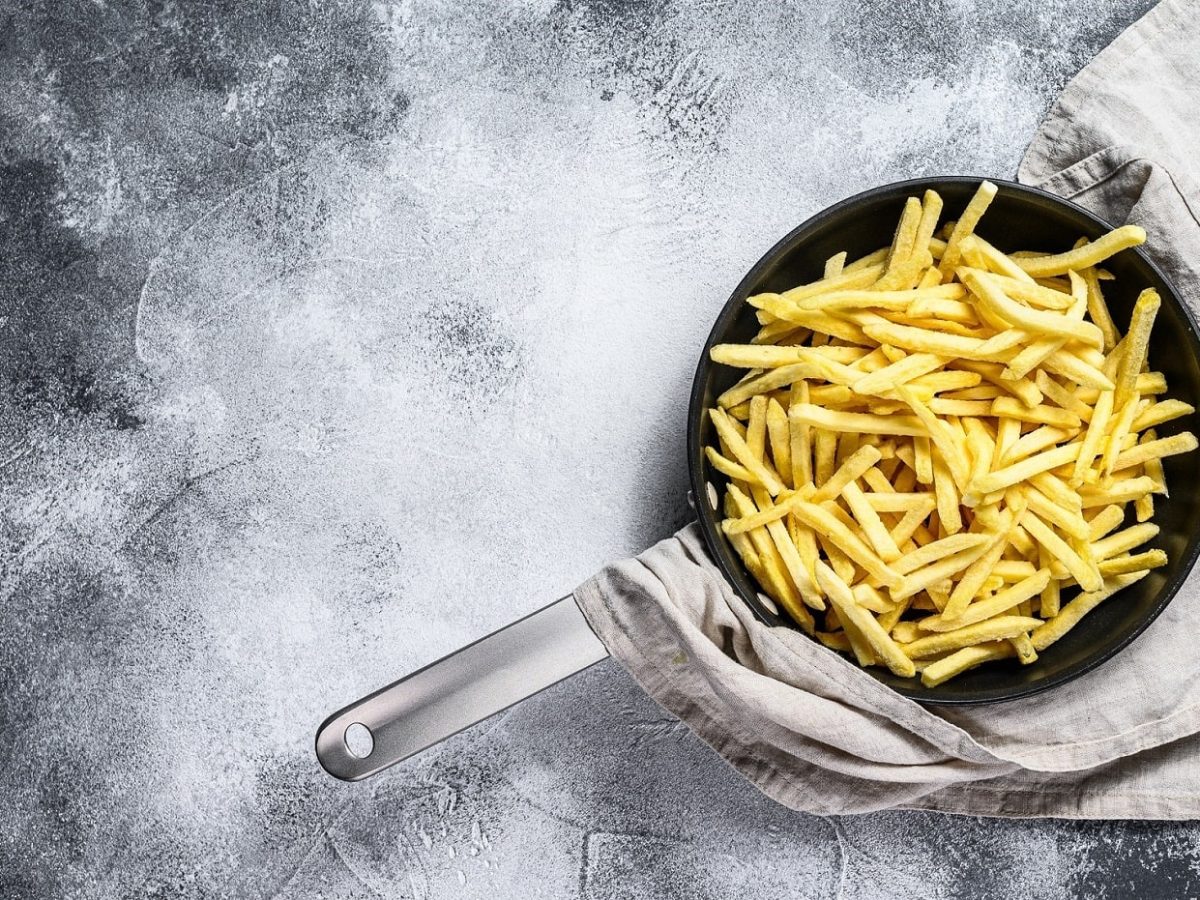 Pommes in einer gusseisernen Pfanne auf dunklem Untergrund umrundet von Rosmarin und Pfefferkörnern.