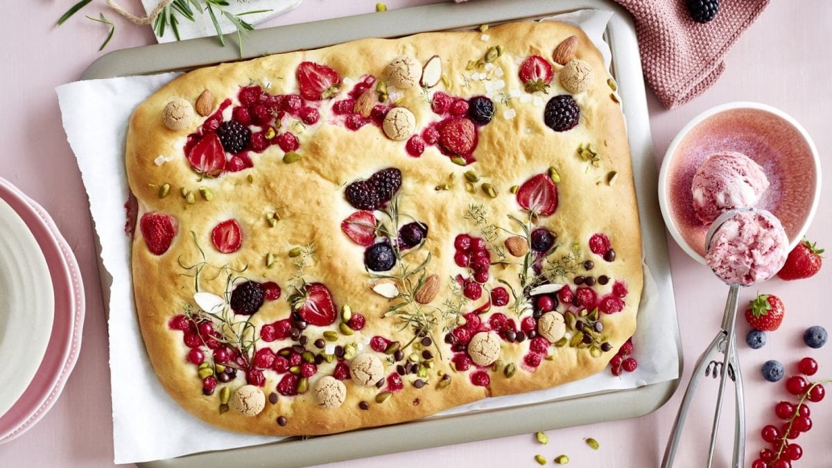 Auf einem Blech liegt eine süße Garten-Focaccia. Sie ist so dekoriert, dass sie wie ein Blumengarten aussieht.