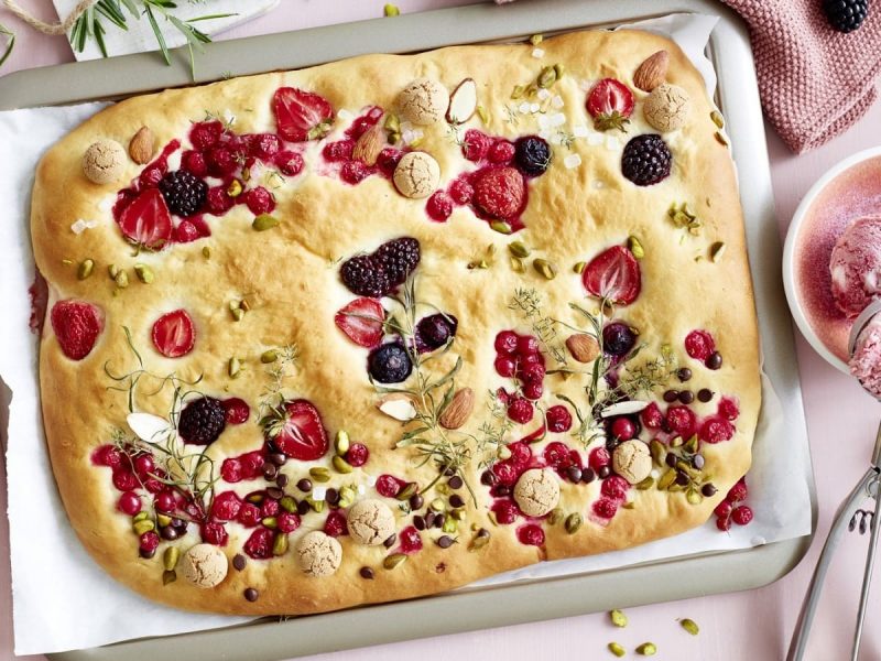 Auf einem Blech liegt eine süße Garten-Focaccia. Sie ist so dekoriert, dass sie wie ein Blumengarten aussieht.