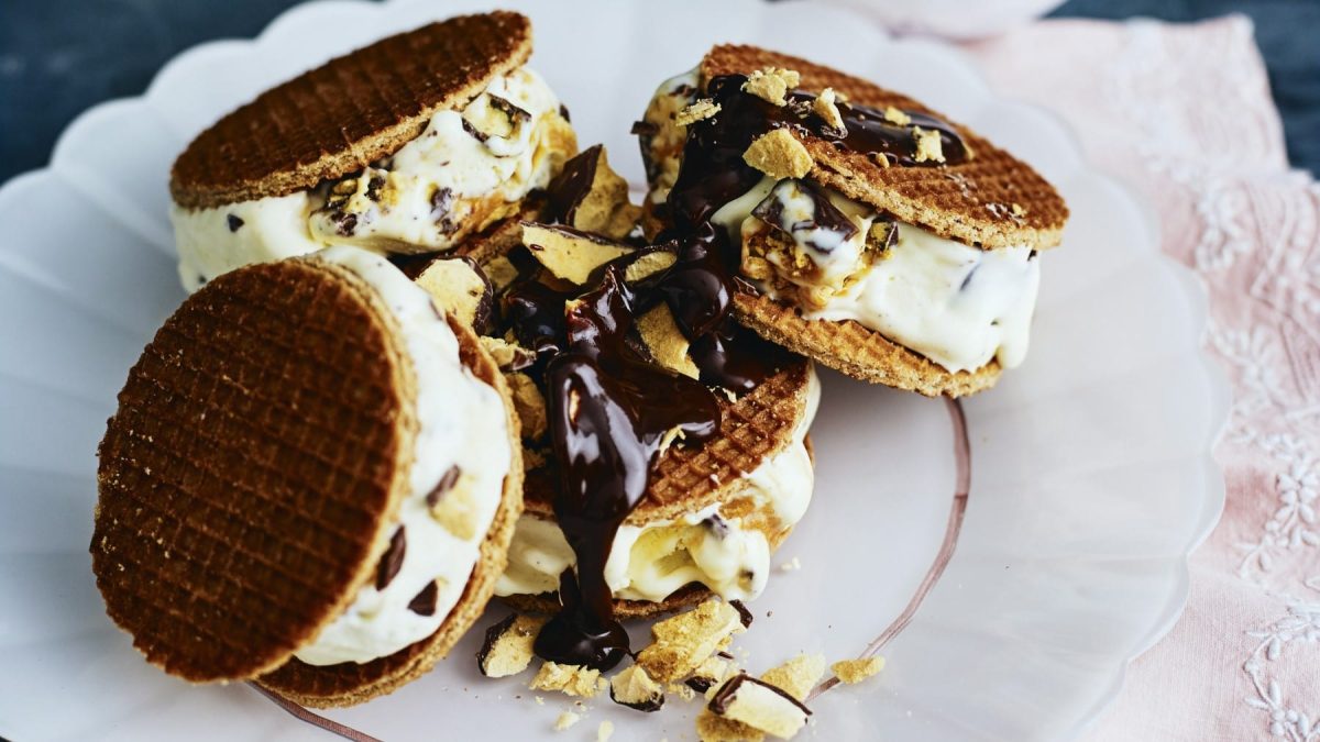 Waffel-Honeycomb-Eissandwiches, garniert mit zerbröselten Eiswaffeln und serviert auf einem wei0en Tisch auf einem rosa Untergrund.