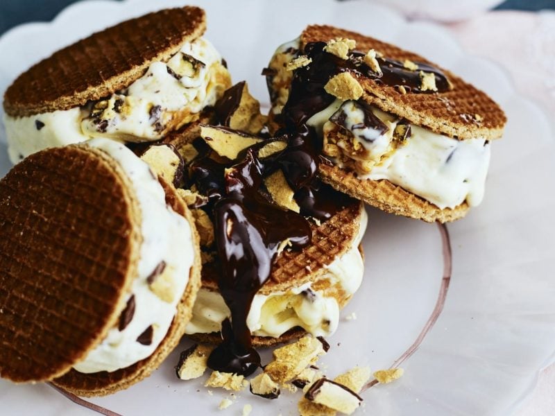 Waffel-Honeycomb-Eissandwiches, garniert mit zerbröselten Eiswaffeln und serviert auf einem wei0en Tisch auf einem rosa Untergrund.