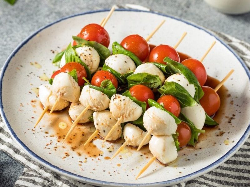 Ein Teller mit vier Caprese-Spießen liegen auf einem Tuch.