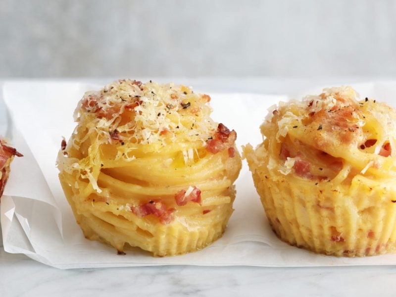 Drei Carbonara-Muffins auf einem hellgrauen Tisch mit einer weißen Serviette und hellgrauem Hintergrund.