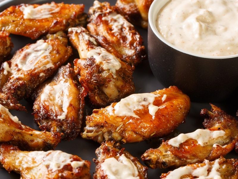 Chicken Wings vom Grill mit Rub und Alabama White Sauce auf schwarzem Teller aus der Draufsicht.