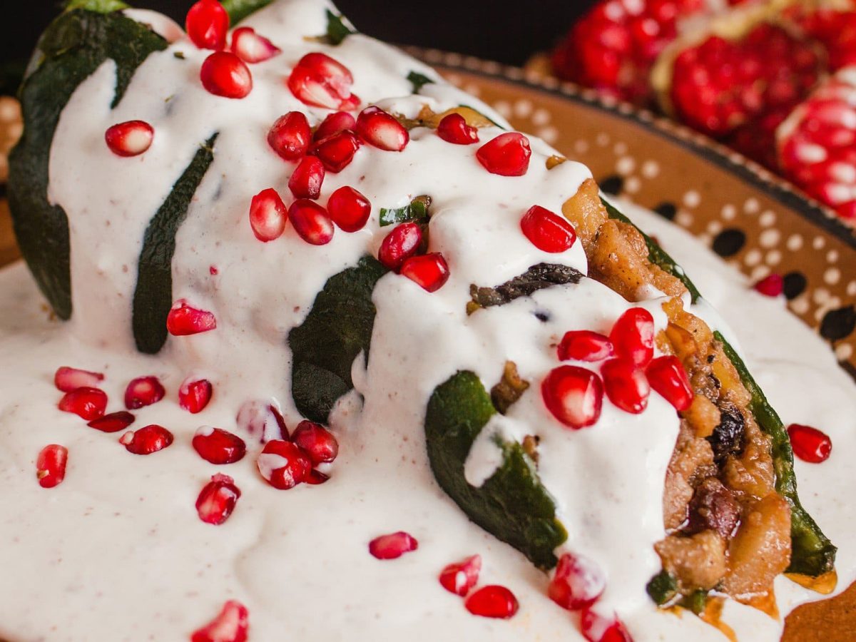 Chiles en nogada gefüllte mexikanische Paprika auf buntem Teller. Daneben Granatapfel. Draufsicht.