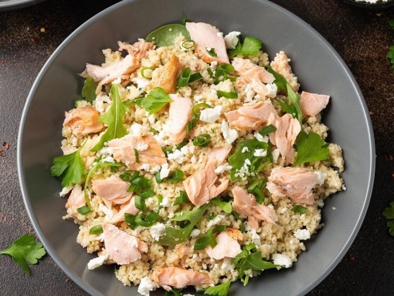 Ein Couscous-Salat mit Lachs & Feta steht auf einem dunklem Untergrund.