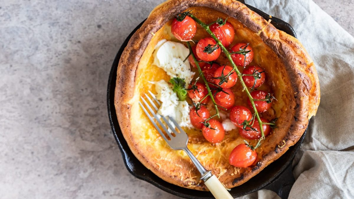 Eine gusseiserne Pfanne mit einem Dutch Baby mit Tomate und Mozzarella.