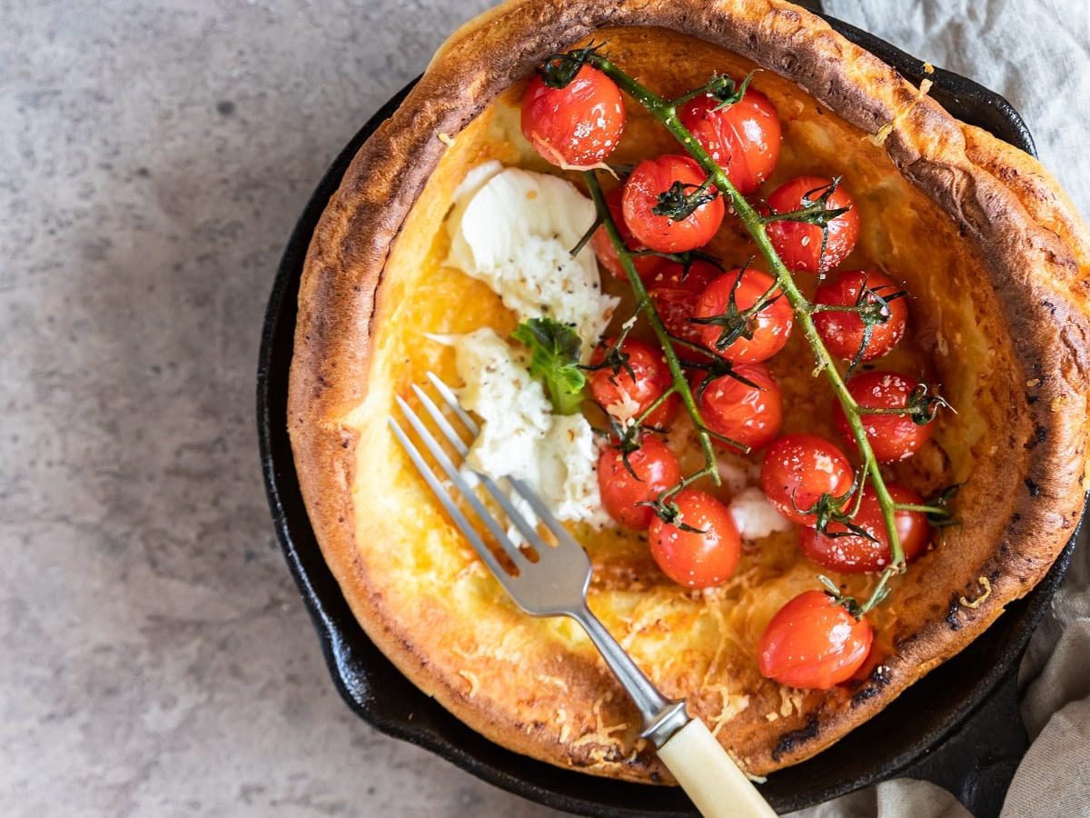 Eine gusseiserne Pfanne mit einem Dutch Baby mit Tomate und Mozzarella.