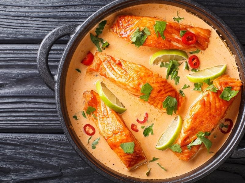 Rotes Curry mit Lachsfilet in einem schwarzen Topfauf schwarzem Hintergrund