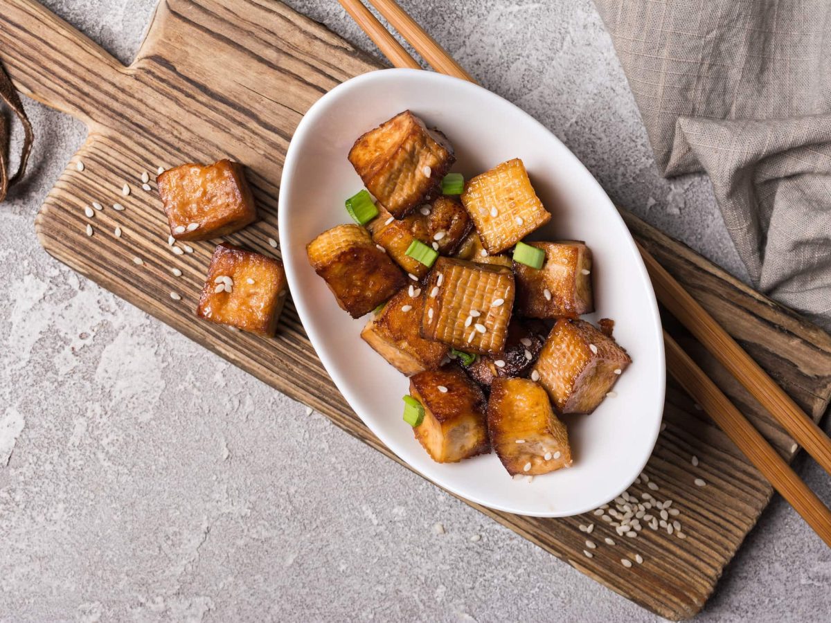 Knuspriger Tofu in weißem teller auf braunem Holzbrett.