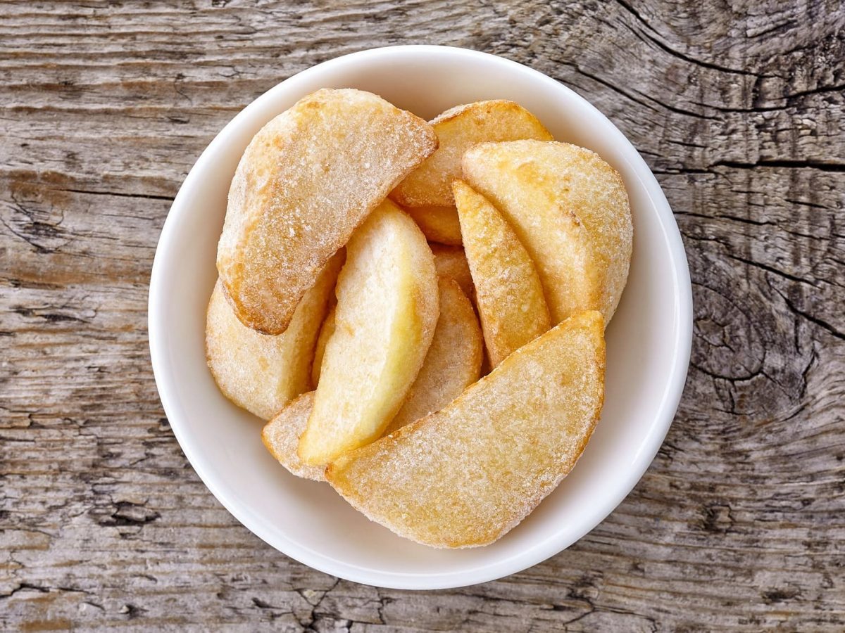 Gefrorene Kartoffeln in weißer Schüssel auf Holzplatte.