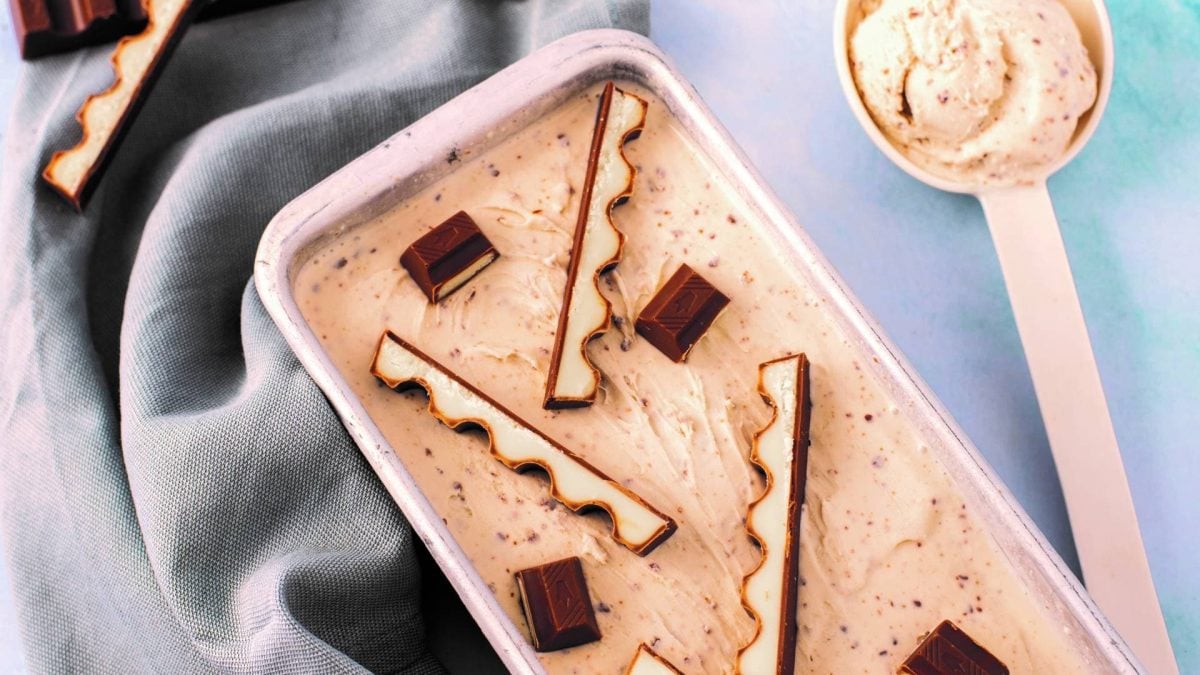 Kinderschokolade-Eis in einer Kastenform, mit Stückchen von Kinderschokolade belegt, daneben ein Eislöffel.