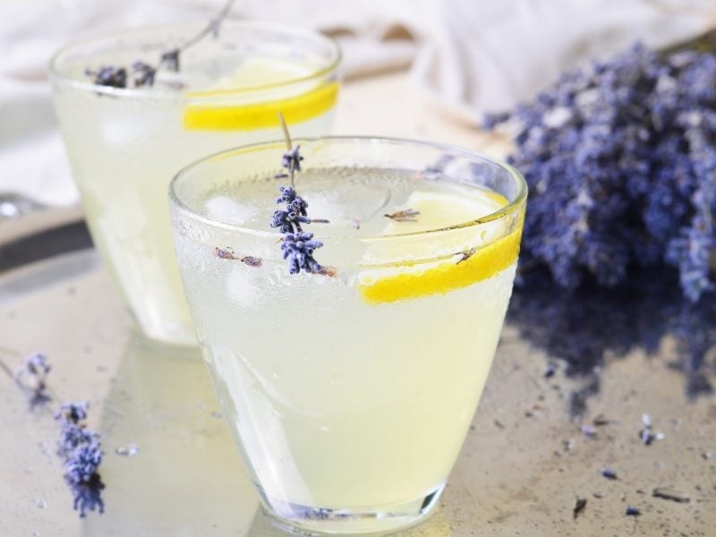 Zwei Gläser der Limonade mit Lavendelblüten auf einem Silbertablett und hellem Hintergrund. Ebenfalls im Hintegrund ist ein ganzer Strauß Lavendel.