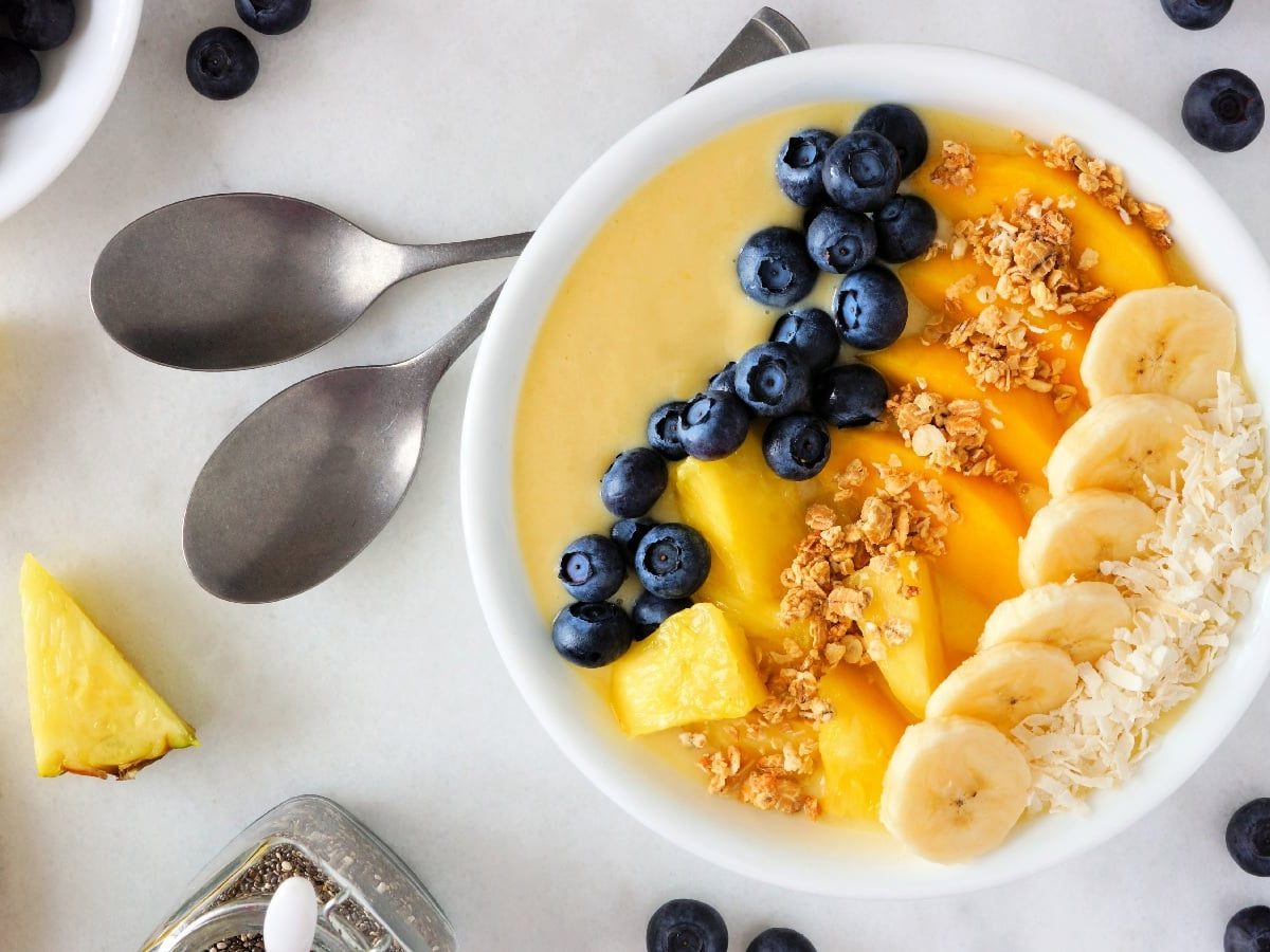 Mango-Smoothie-Bowl in einer weißen Schale neben zwei Löffeln