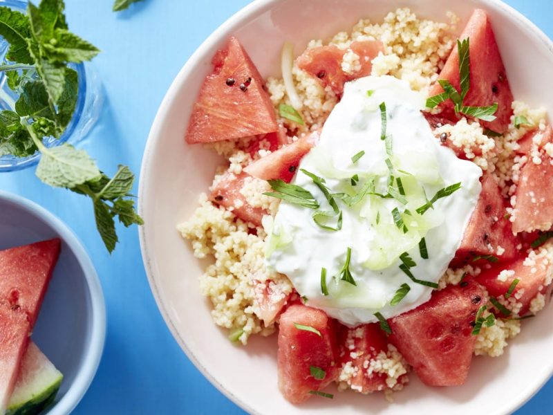 Melonensalat mit Couscous und Gurke, getoppt mit griechischem Joghurt und Minze. Draufsicht.