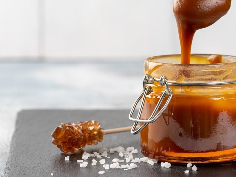 Ein Weckglas mit Salted-Caramel-Aufstrich und Meersalz auf einer schwarzen Schieferplatte.