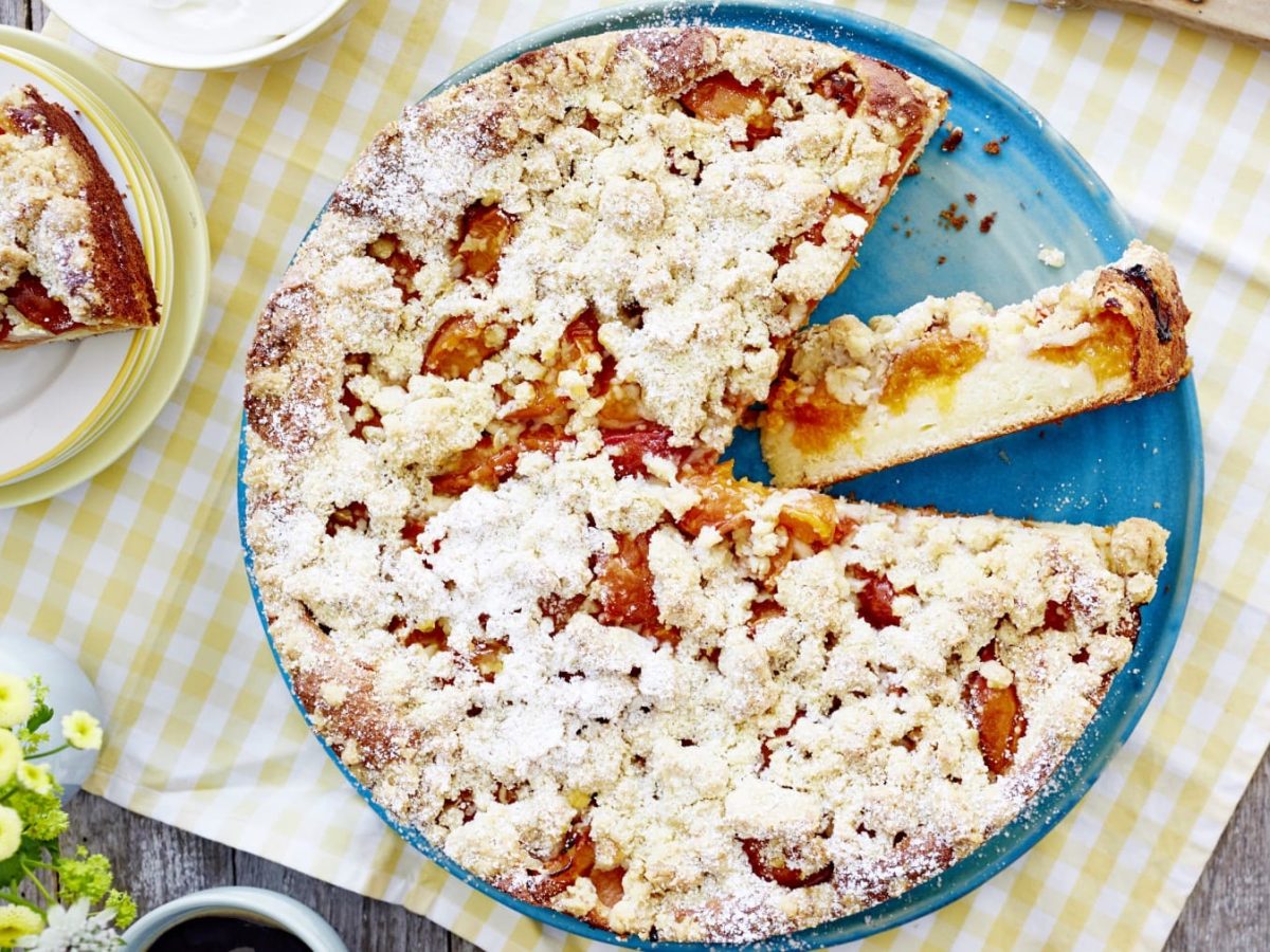 Skyr-Aprikosen-Streuselkuchen auf einem blauen Teller auf einer weißgelb karierten Tischdecke.