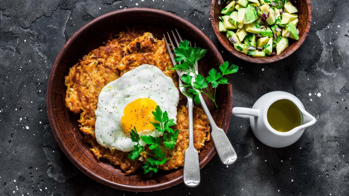 eine schale Süßkartoffel-Rösti mit Spiegelei und Avocado-Salsa steht auf einem dunklen untergrund.