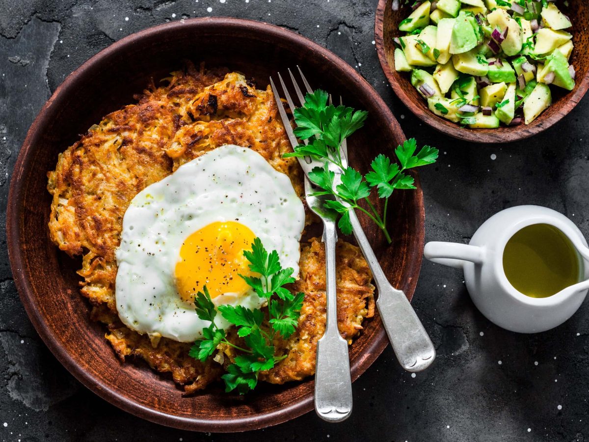 eine schale Süßkartoffel-Rösti mit Spiegelei und Avocado-Salsa steht auf einem dunklen untergrund.