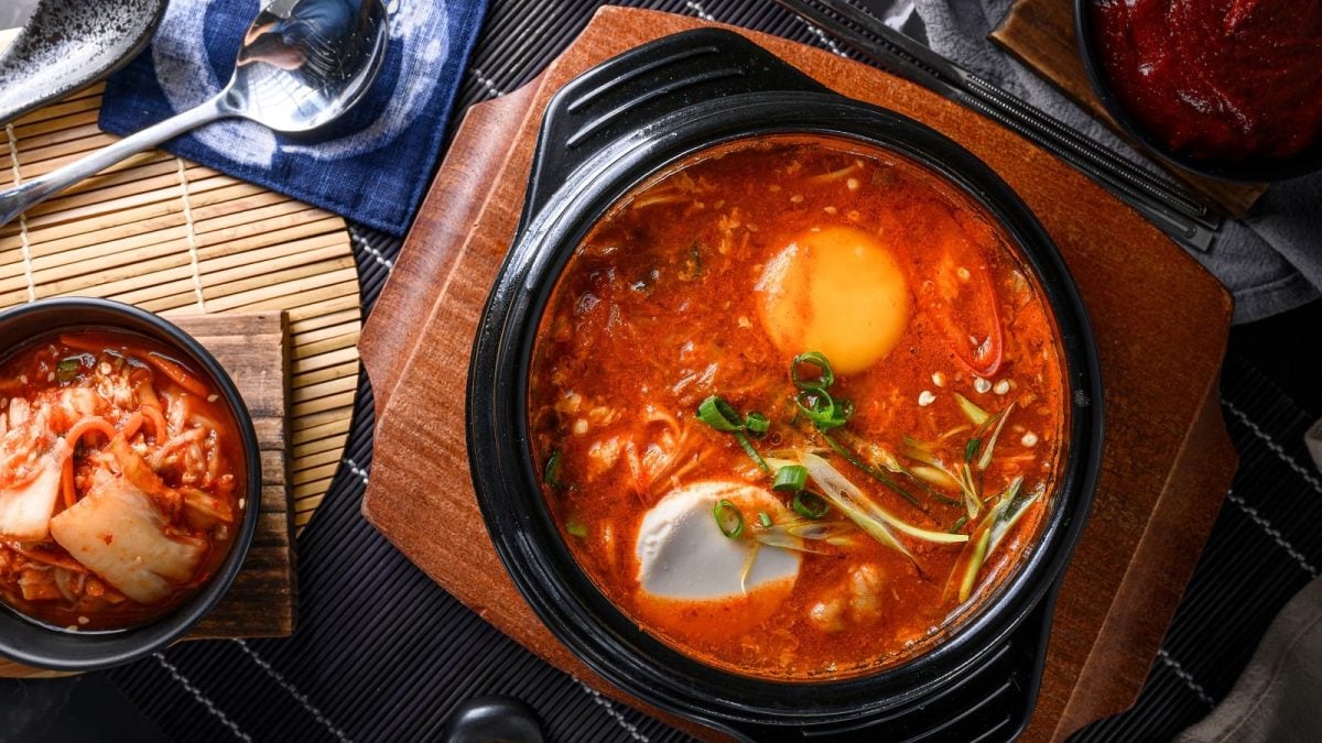 Ein schwarzer Topf mit Sundubu Jjigae neben Kimchi.