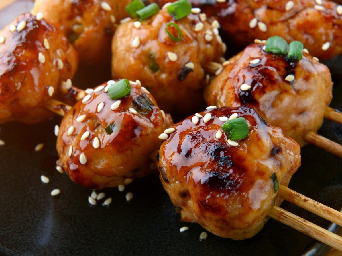 Tsukune Yakitori auf schwarzer Platte auf Holztisch. Draufsicht.