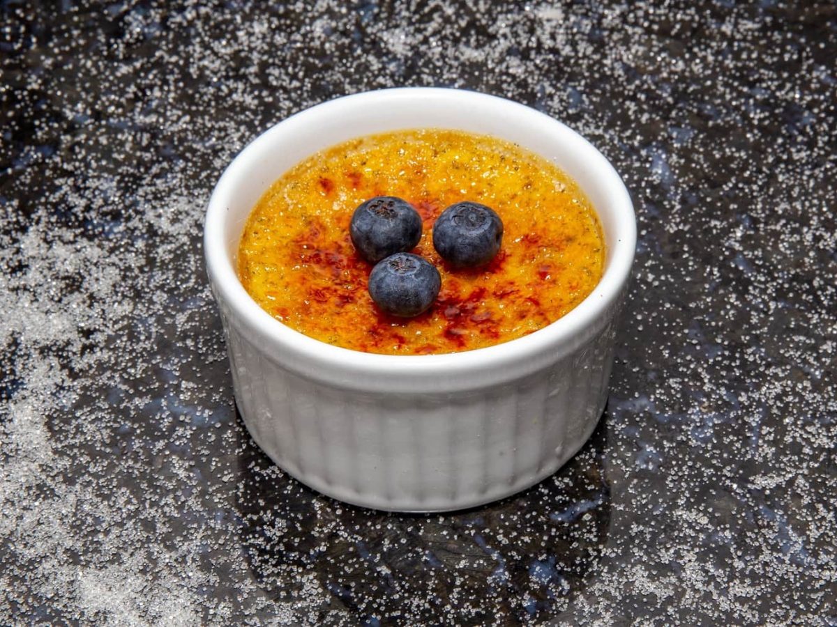 Eine kleine weiße Schale vegane Crème brûlée mit drei Heidelbeeren.