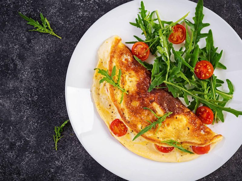 Ein veganes Omelett mit Tomaten und Rucola auf einem Teller in der Draufsicht.