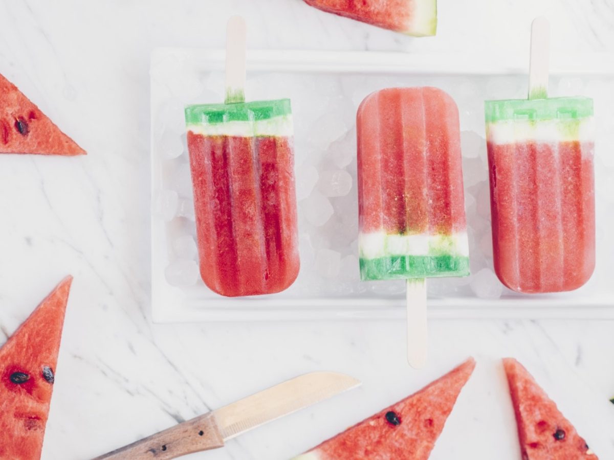 Wassermelonen Popsicles in einer Schale mit Eiswürfeln. Daneben liegen Wassermelonenscheiben.