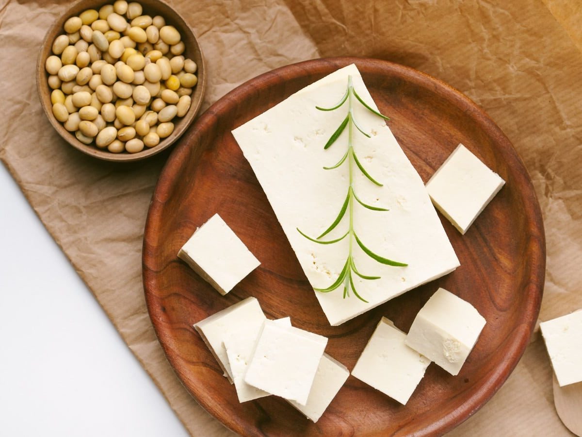 Ein Holztablett mit frischem Tofu auf einem braunen Papier neben Sojabohnen