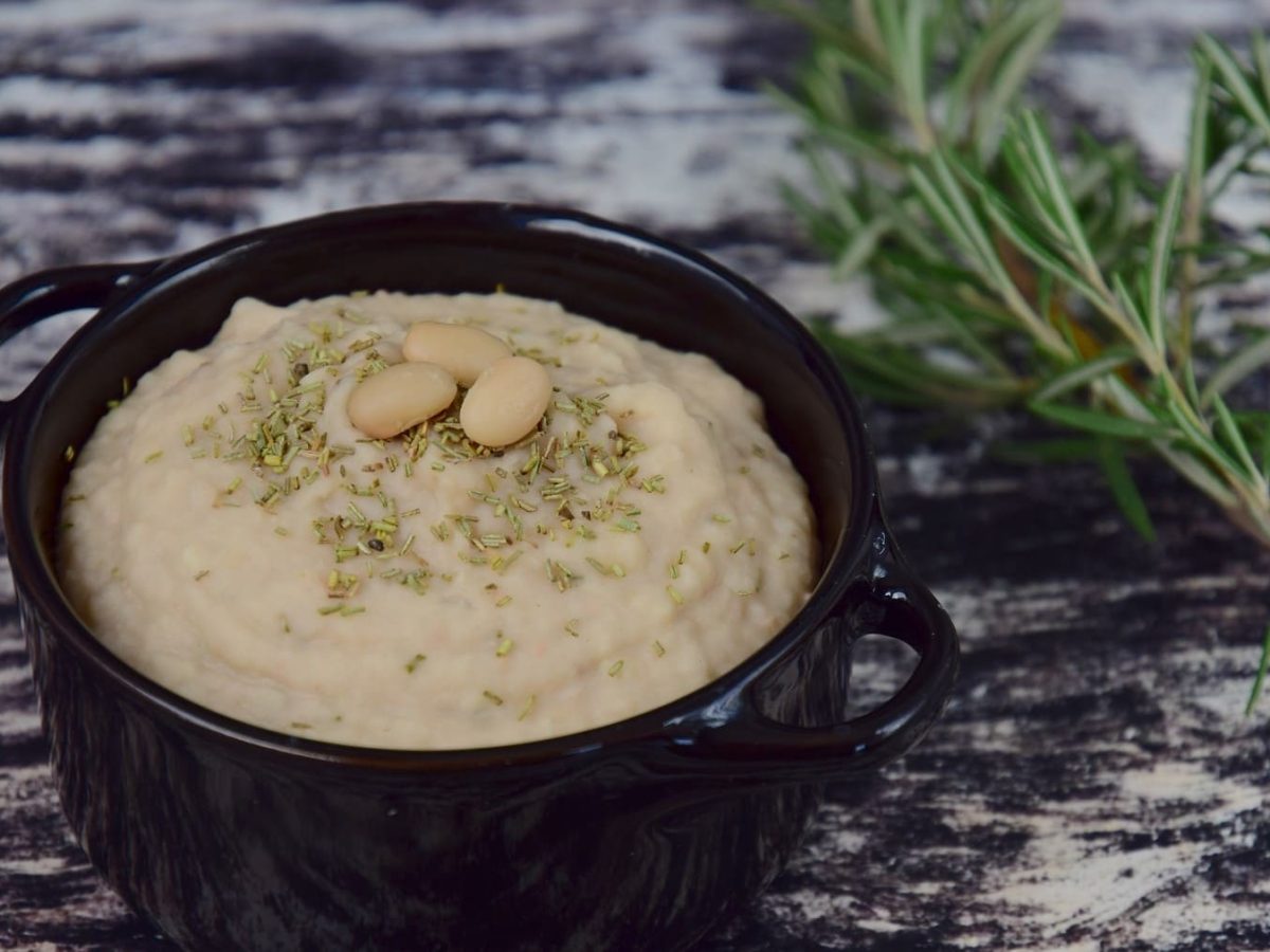 Cremige Bohnen-Paste mit Knoblauch, garniert mit Rosmarin und serviert in einer kleinen schwarzen Schale auf einem Marmortisch.