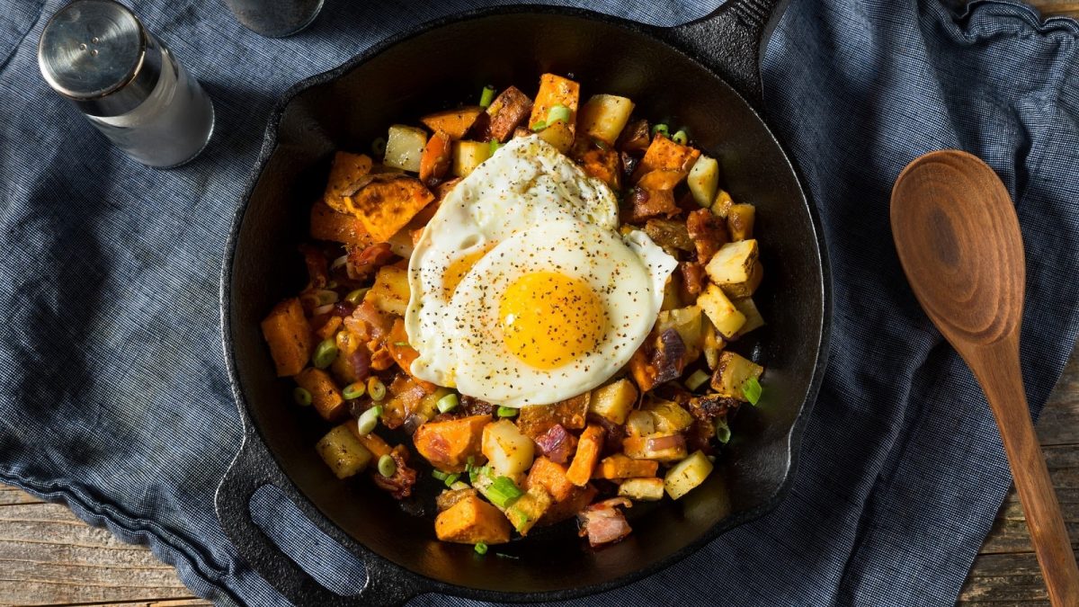 Eine schwarze Pfanne mit Süßkartoffel-Pfanne auf einem dunkelblauen Küchentuch.