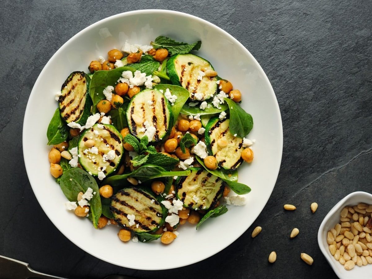 Ein weißer Teller mit gegrillter Zucchini mit Kichererbsen und Feta.