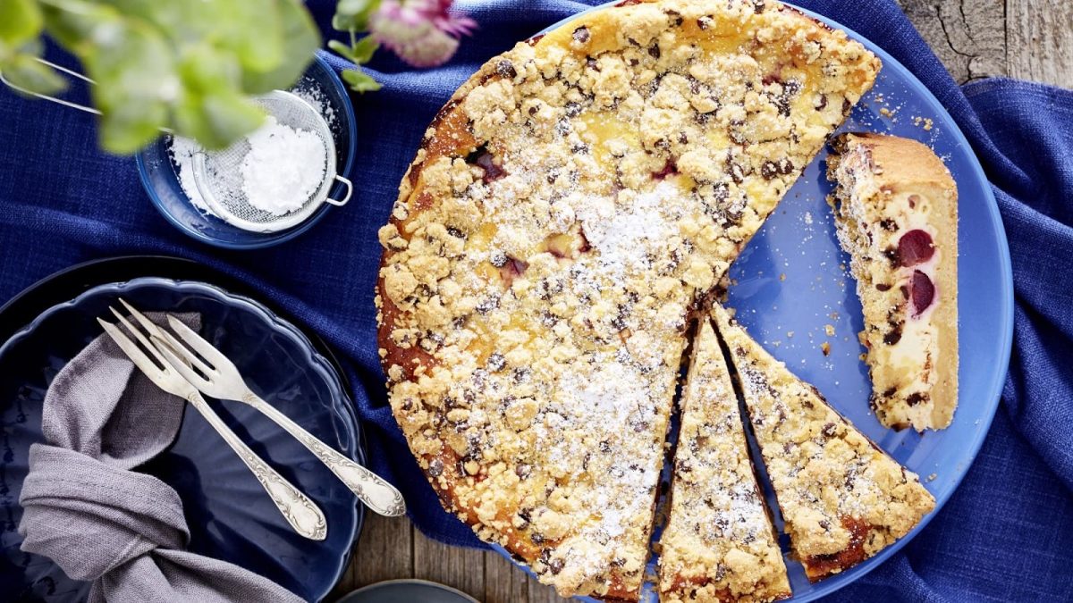 Auf einem blauen Teller liegt ein Käse-Kirsch-Streuselkuchen. Er ist mit Puderzucker bestreut.