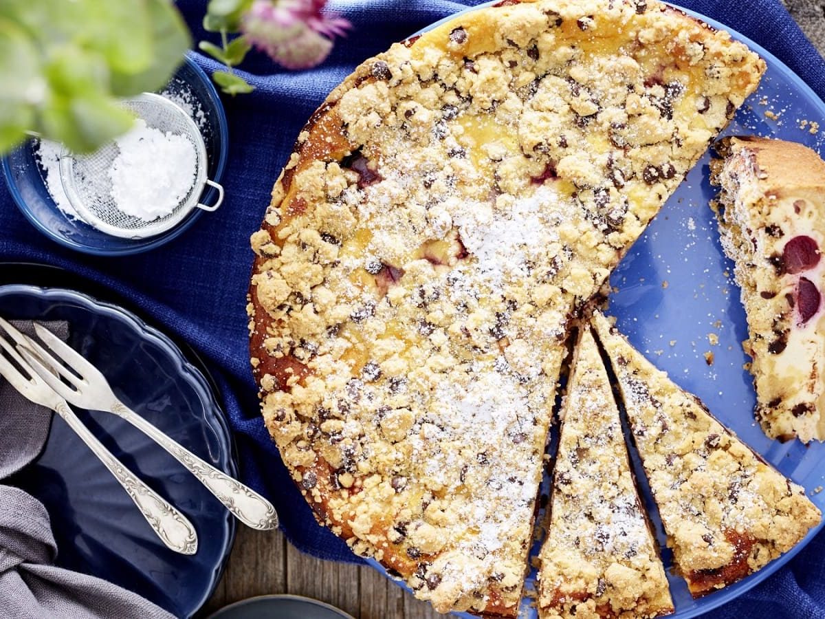 Auf einem blauen Teller liegt ein Käse-Kirsch-Streuselkuchen. Er ist mit Puderzucker bestreut.