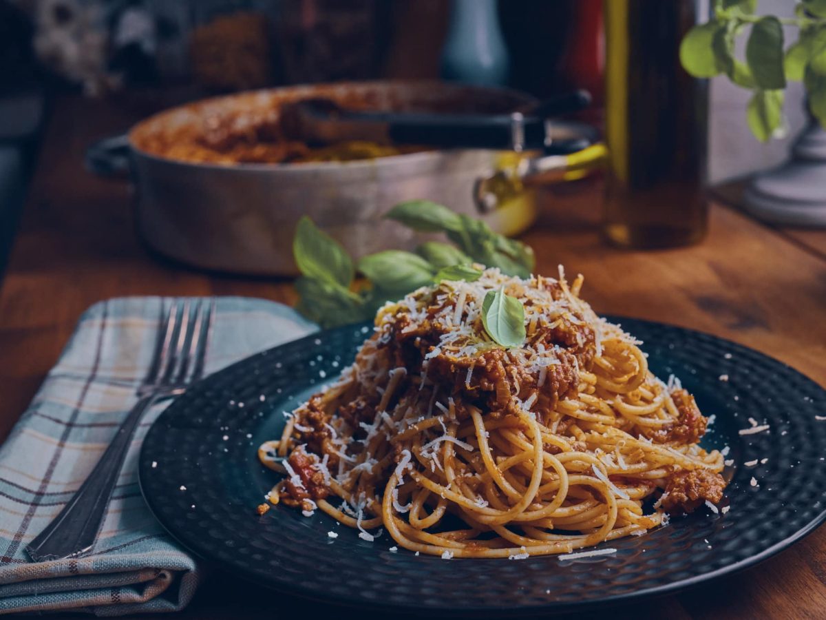 Spaghetti Bolognese bestreut mit Kräutern und Parmesan auf dunklem Teller