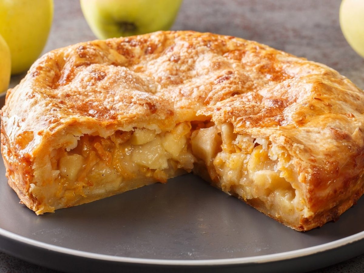 Angeschnittener Apple-Cheddar-Pie, gefüllt mit Apfelstücken und überbacken mit einer Käsekruste, serviert auf einem grauen großen Teller auf einem einfachen schwarzen Tisch.