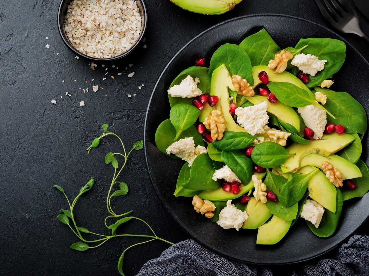 Ein schwarzer Teller mit Avocado-Salat, auf schwarzem Hintergrund neben Besteck und frischen Zutaten.