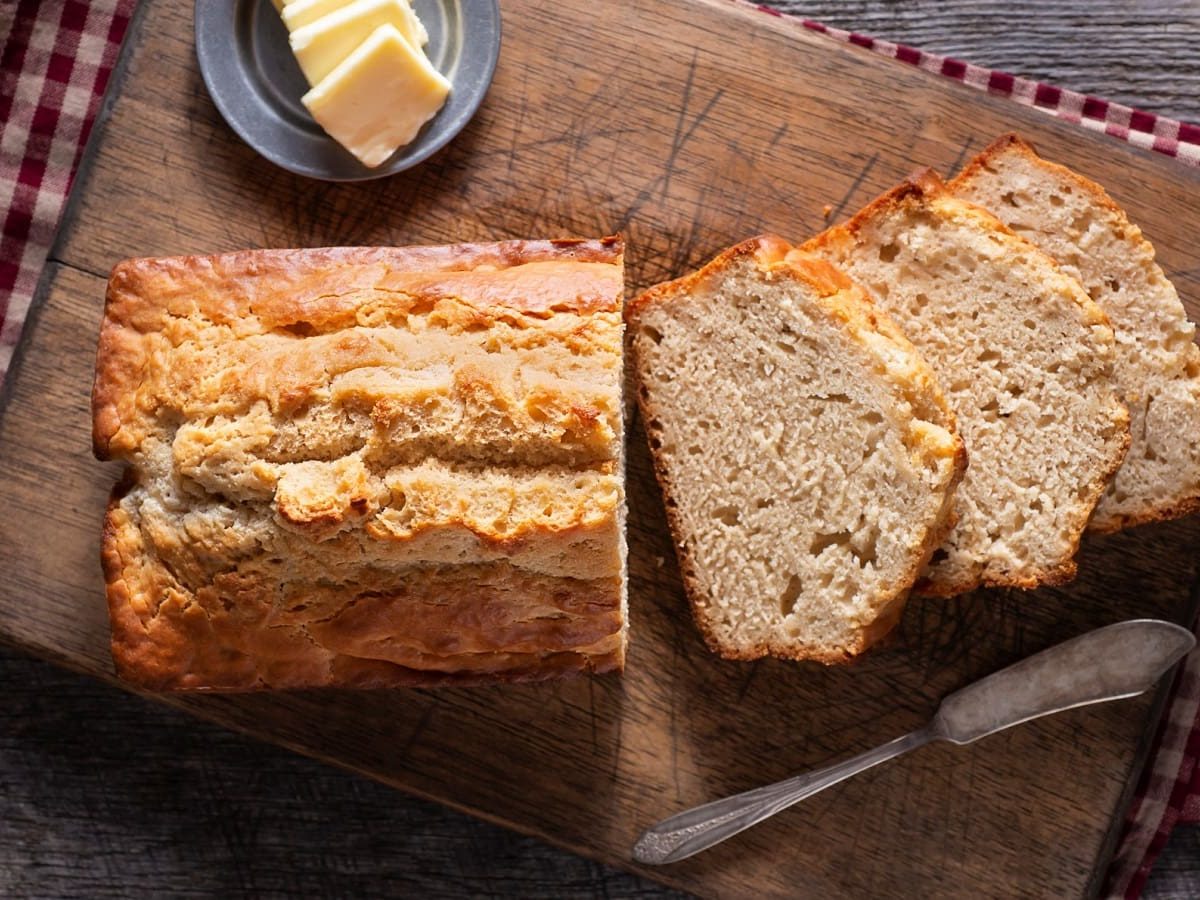 Bierbrot in Kastenform auf einem Holzbrett neben Butter