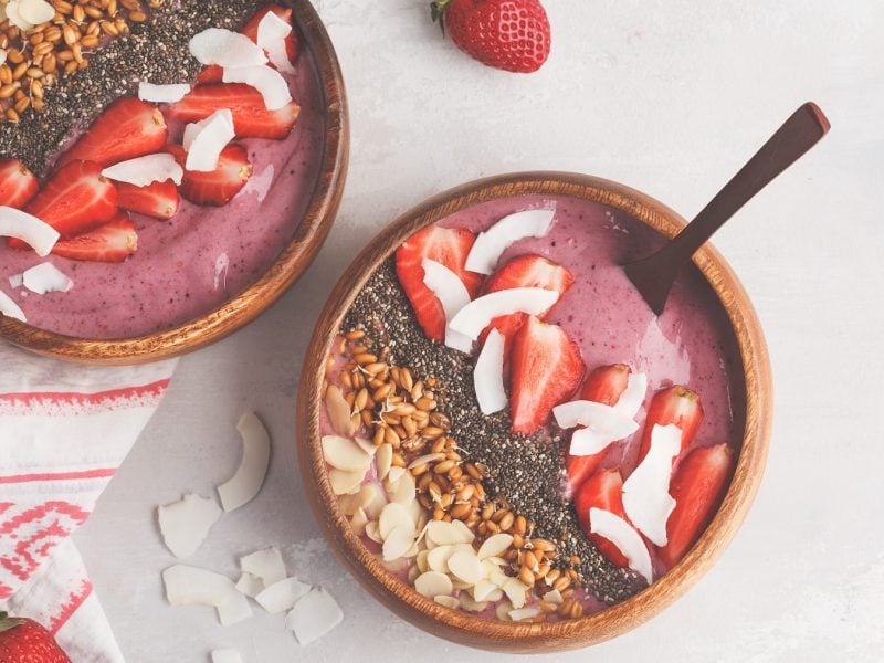 Zwei Schalen Erdbeer-Smoothie-Bowl mit Erdbeeren, Kokoschips, Mandelblätten, in der Draufsicht.