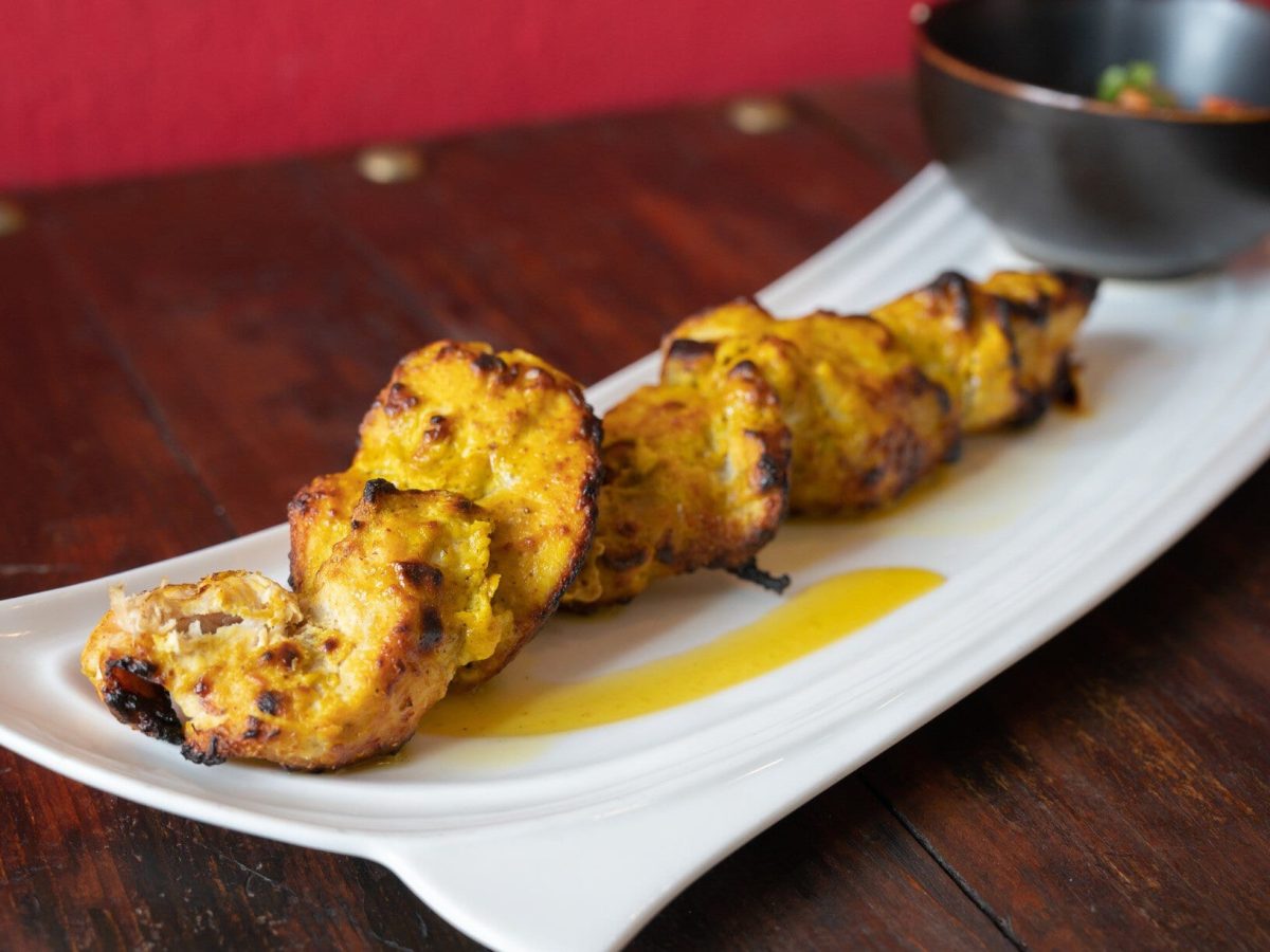 Gegrillte Hähnchenbrust in Zitronen-Knoblauch-Marinade auf weißem Teller und dunklem Untergrund. Daneben Schale mit Curry-Sauce. Frontalansicht.