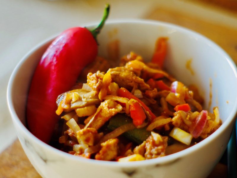 Hackpfanne mit Reis und Halloumi in weißer Schale mit ganzer Chilischote auf Holzbrett. Draufsicht.