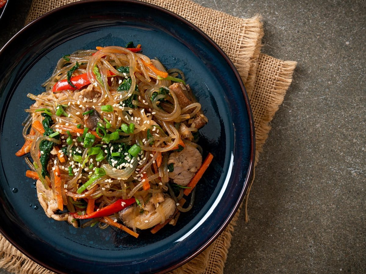 Ein blau-schwarzer Teller mit Japchae auf eine braunen Tuch