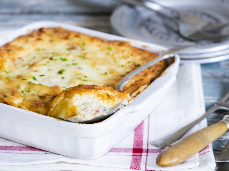 Kartoffel-Soufflé mit Schinken in einer quadratischen Auflaufform. Daneben liegt Besteck.