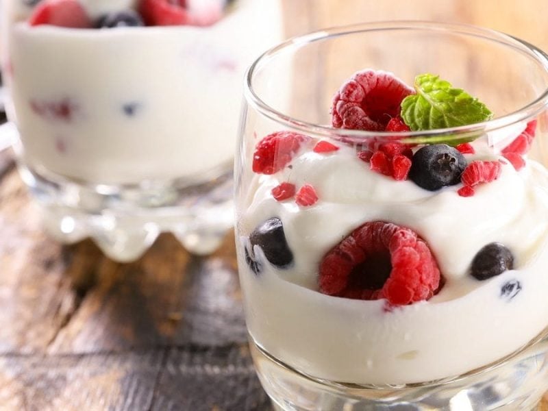 Zwei Gläser Kokos-Joghurt mit Beeren stehen auf einem Holztisch