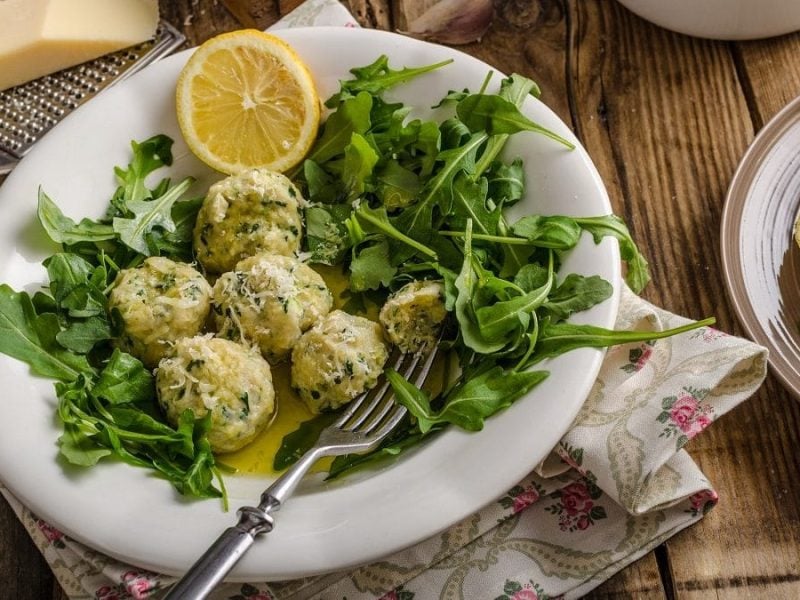 Eine Schüssel Malfatti-Rucola-Salat steht auf einem rustikalen Untergrund.